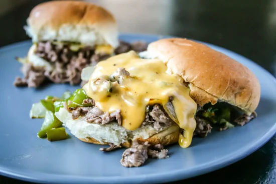Delicious cheesesteak sliders with beef, peppers, onions, and melted cheese on a blue plate.