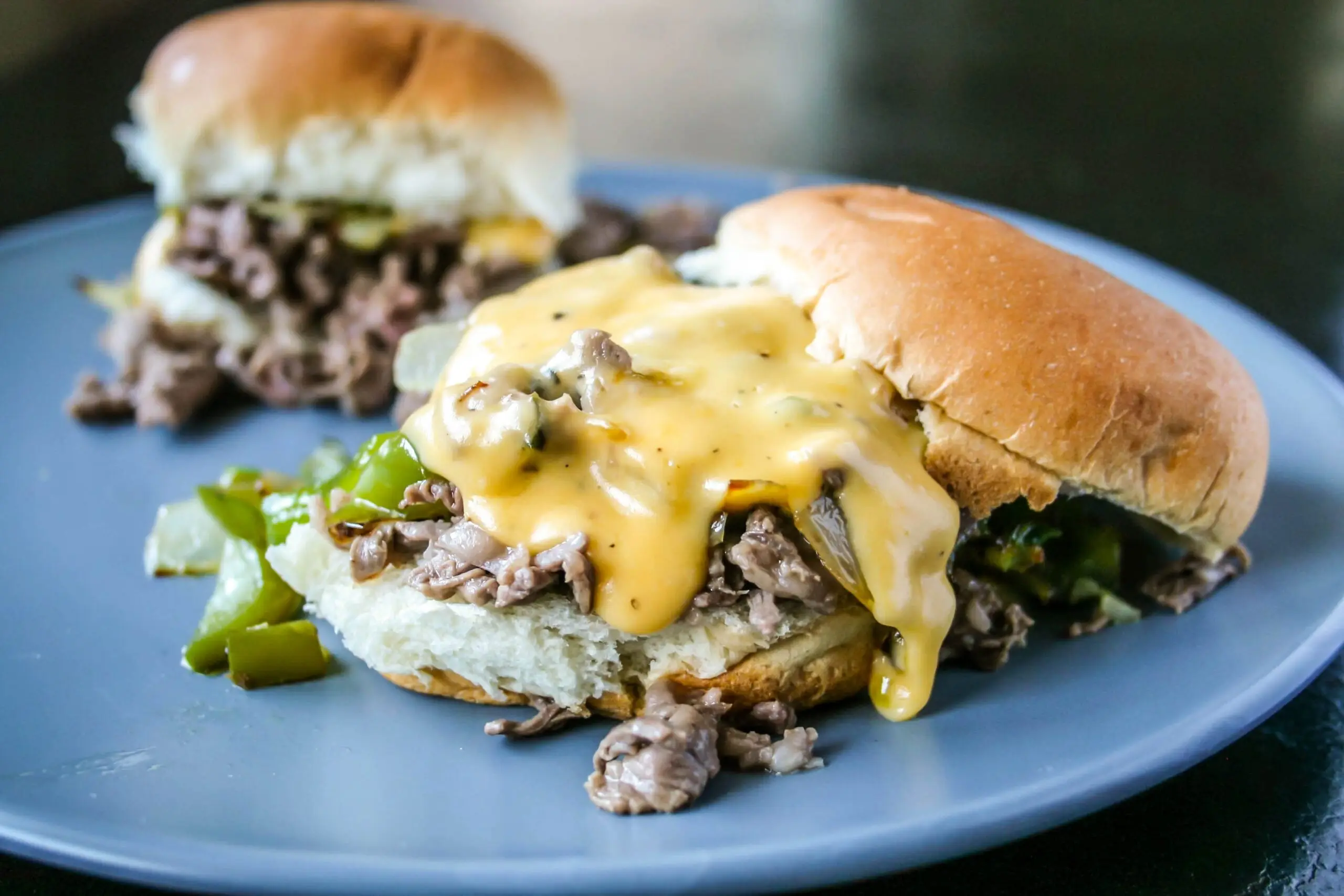 Delicious cheesesteak sliders with beef, peppers, onions, and melted cheese on a blue plate.
