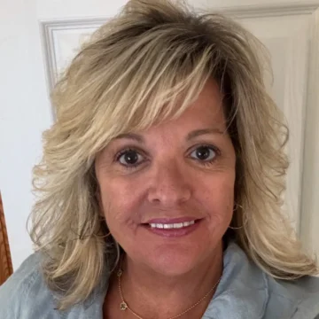 Smiling woman in light blue jacket with blonde hair and hoop earrings, exuding warmth and confidence.